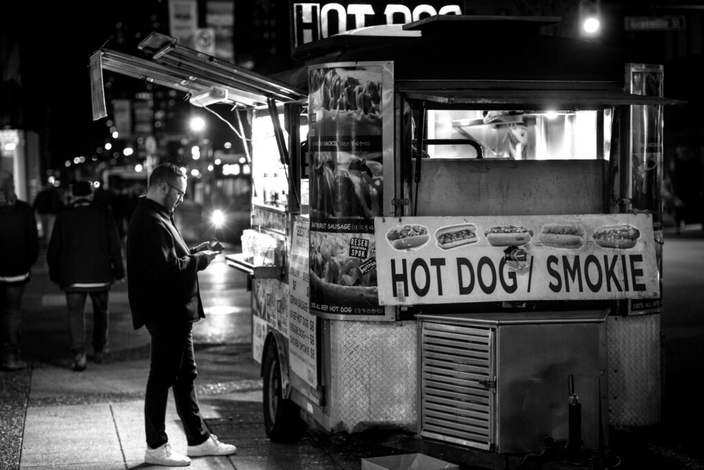Person standing at a hot dog cart shot in Black and White at night.