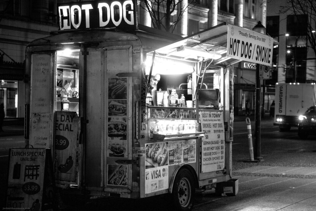 Hot dog cart illuminated at night with staff inside
