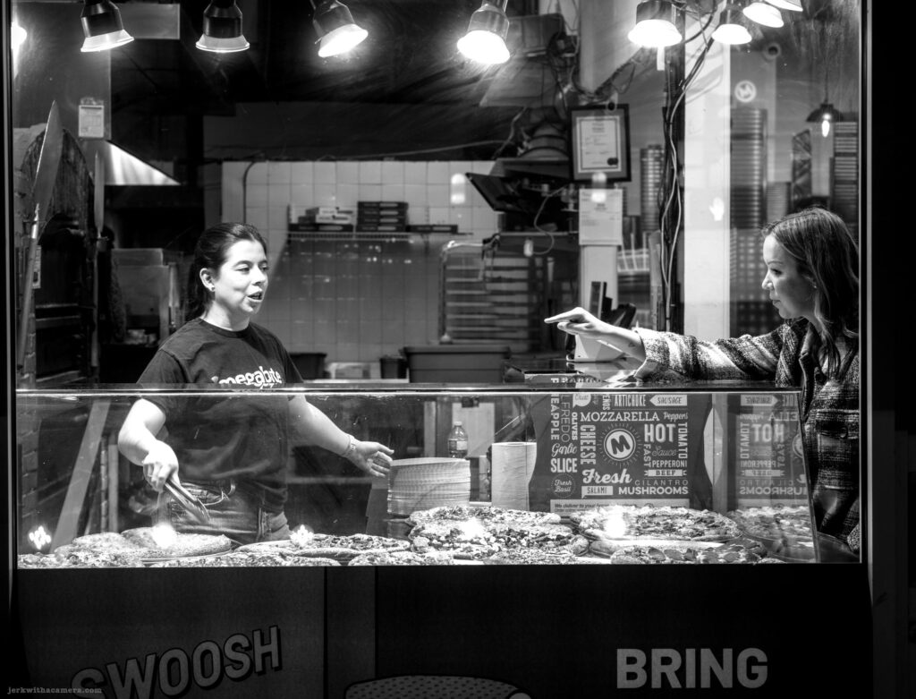 Pizza counter interaction between staff and customer shot in Black and White at night.