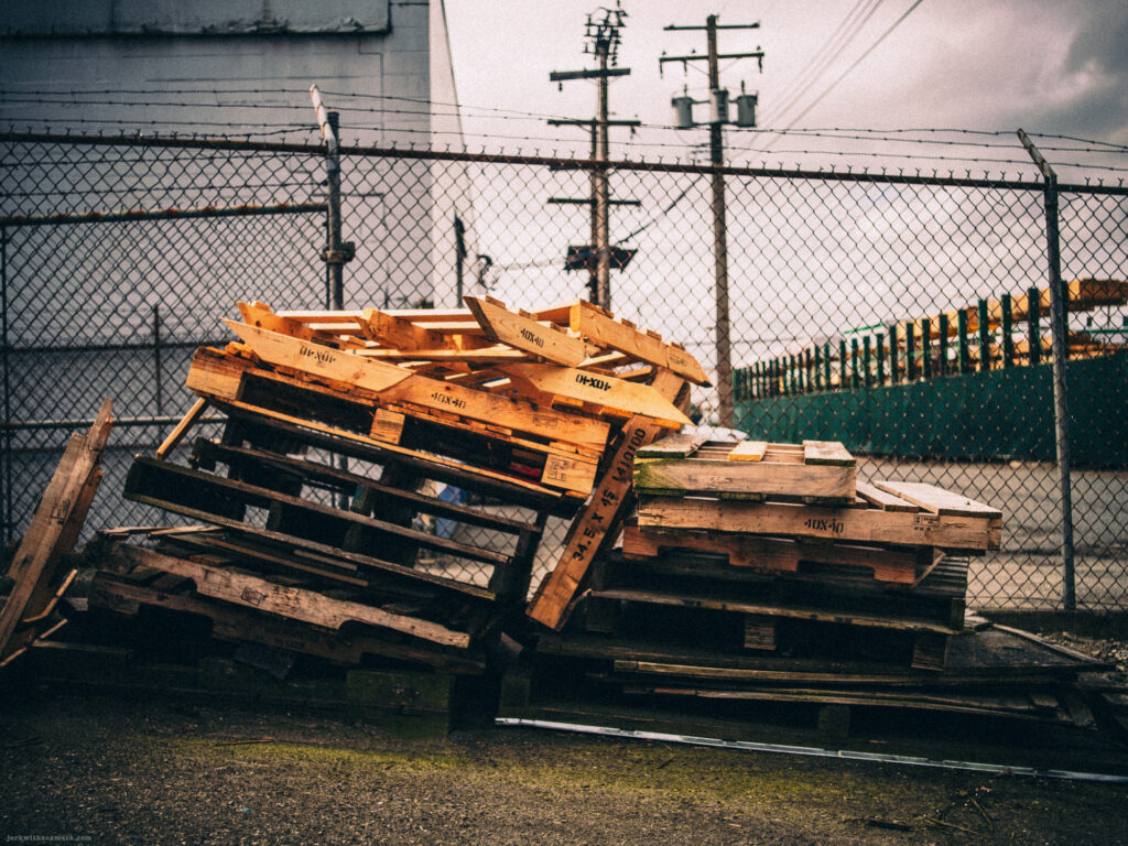 Broken and tilted wooden pallets against a chain-link fence