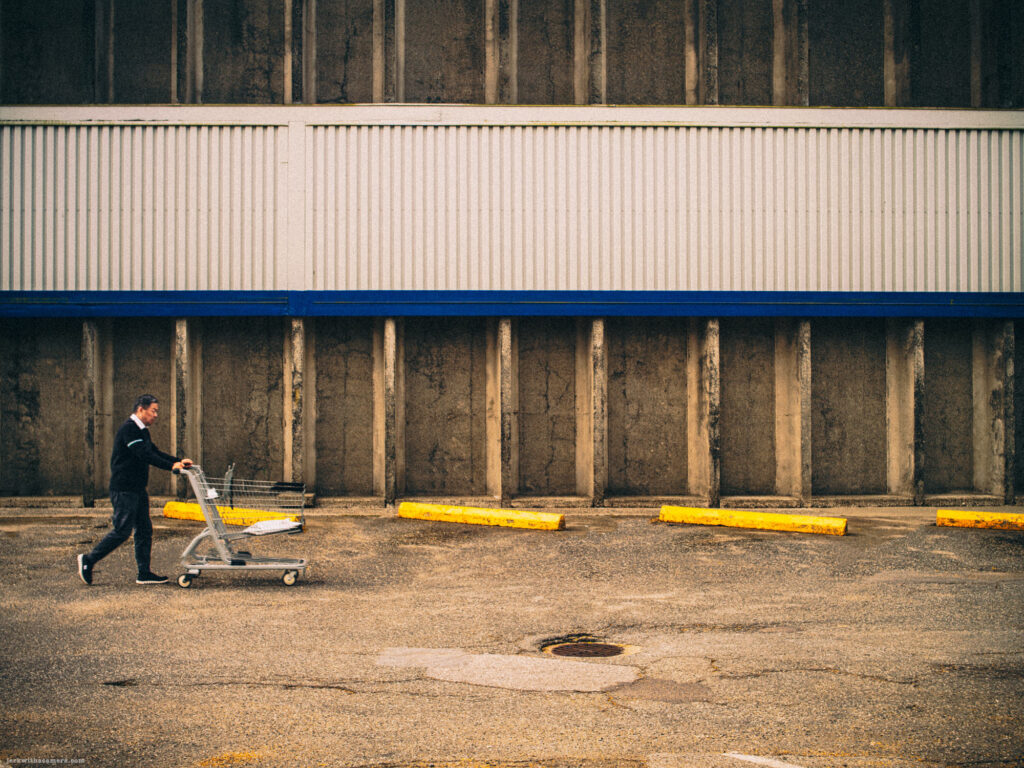 Man pushing shopping cart in front of concrete wall
