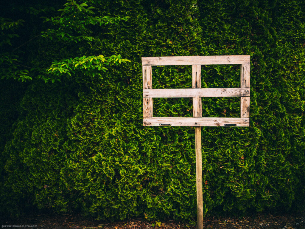 Wooden pallet mounted on post in front of green hedge