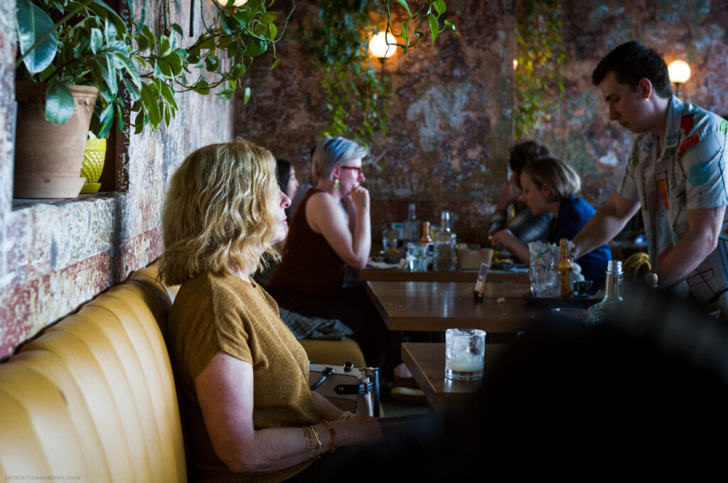 A woman sits at a table in a dimly lit restaurant with other diners in the background.