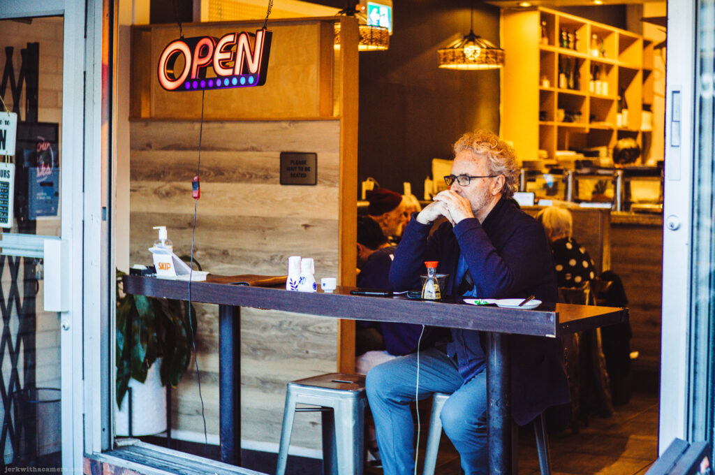 A man sits at a counter in a restaurant with an open sign above him.