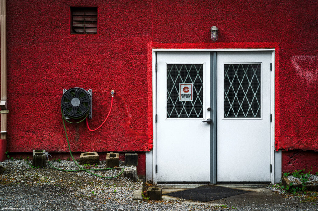 White double doors on red stucco wall with garden hose