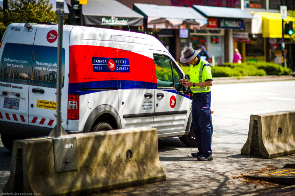 Canada Post worker using a mobile device beside a Canada Post delivery van