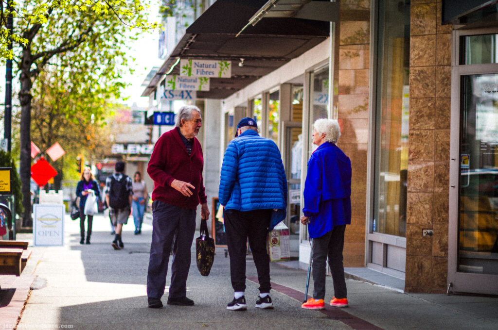 Three older adults having a conversation on the sidewalk outside storefronts