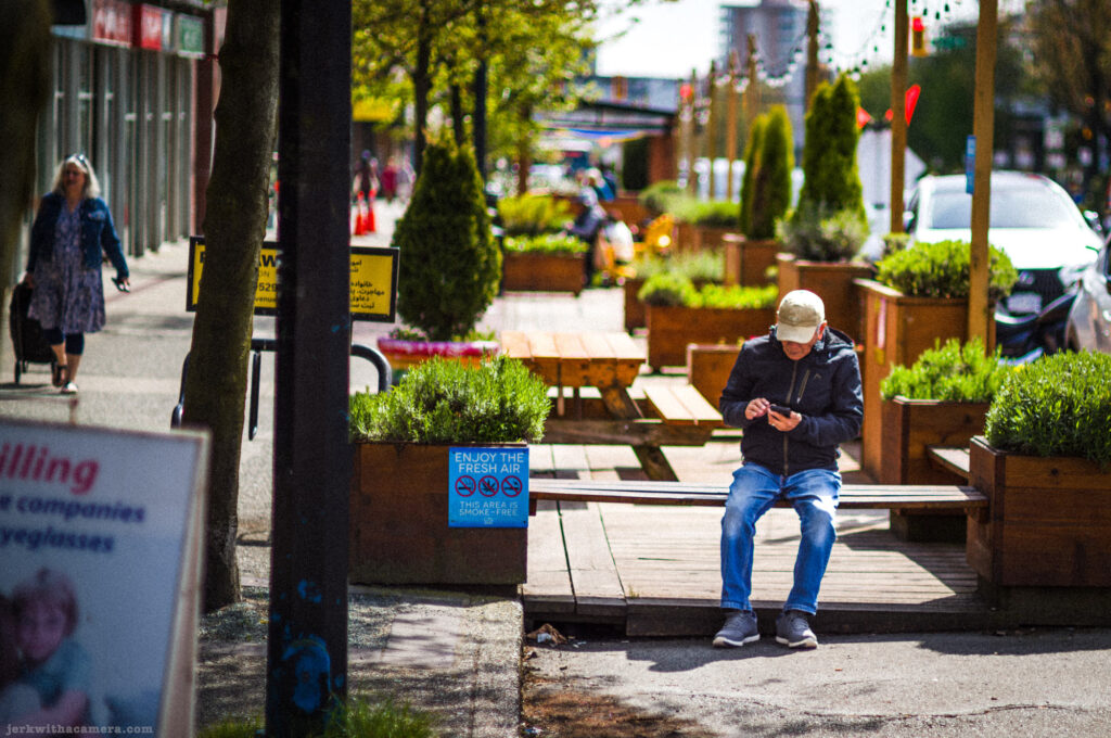 Man sitting alone on a public bench using a phone on a commercial street