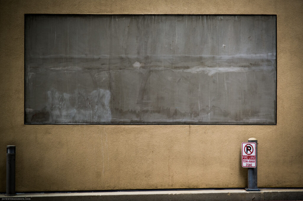 No parking sign beside a large sealed window on a tan wall