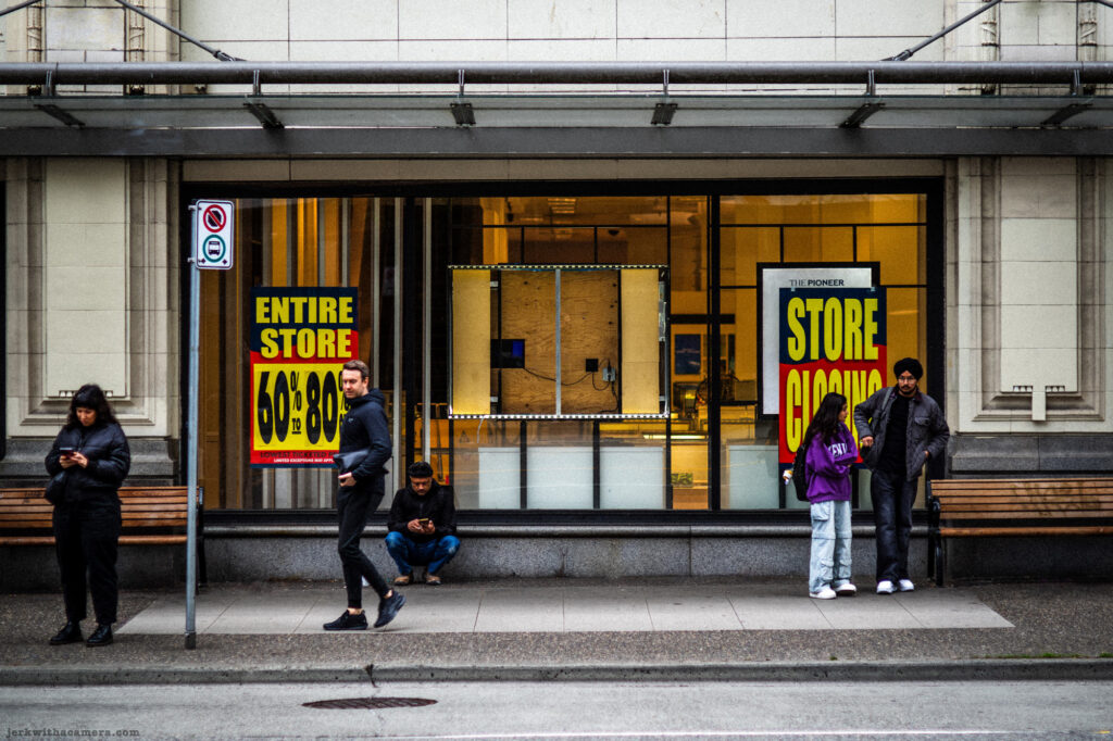 People waiting on the sidewalk in front of a store closing sign