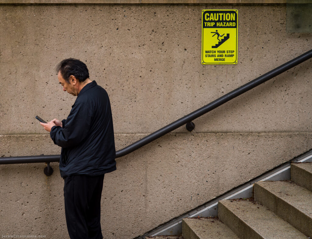 Man looking at phone beside a trip hazard caution sign on a wall
