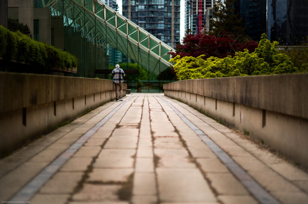 Man walking on elevated path by glass building with highrises in background