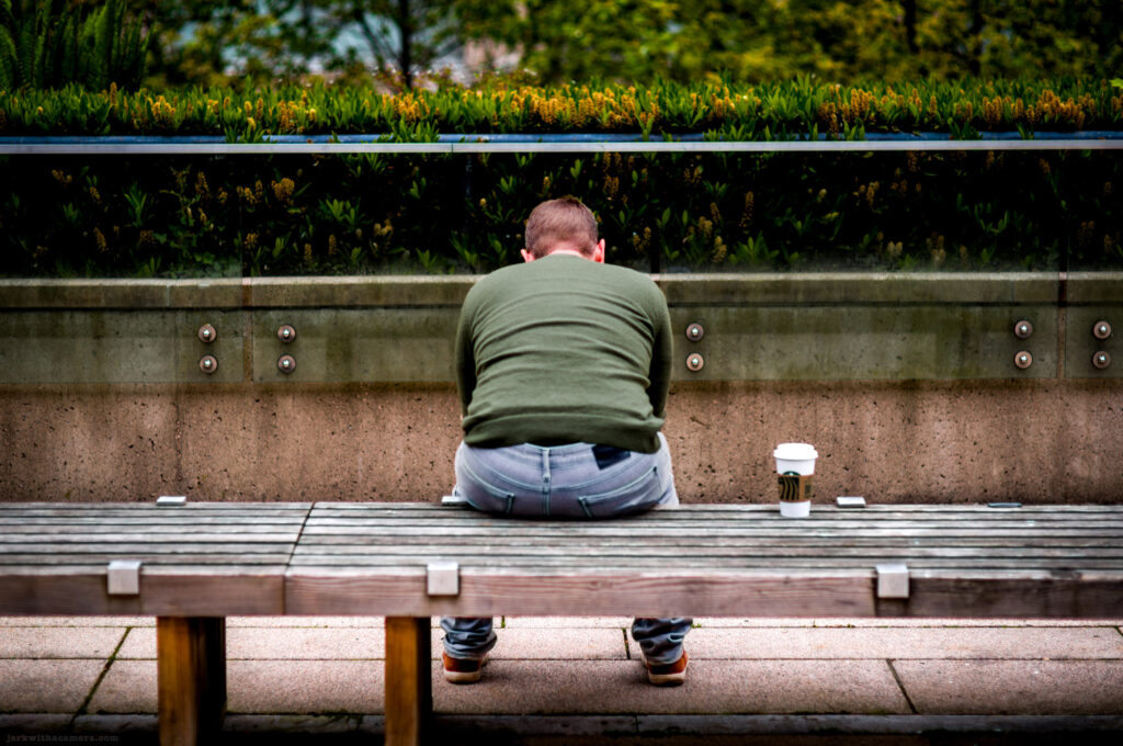 Man sitting on bench facing away with coffee and phone