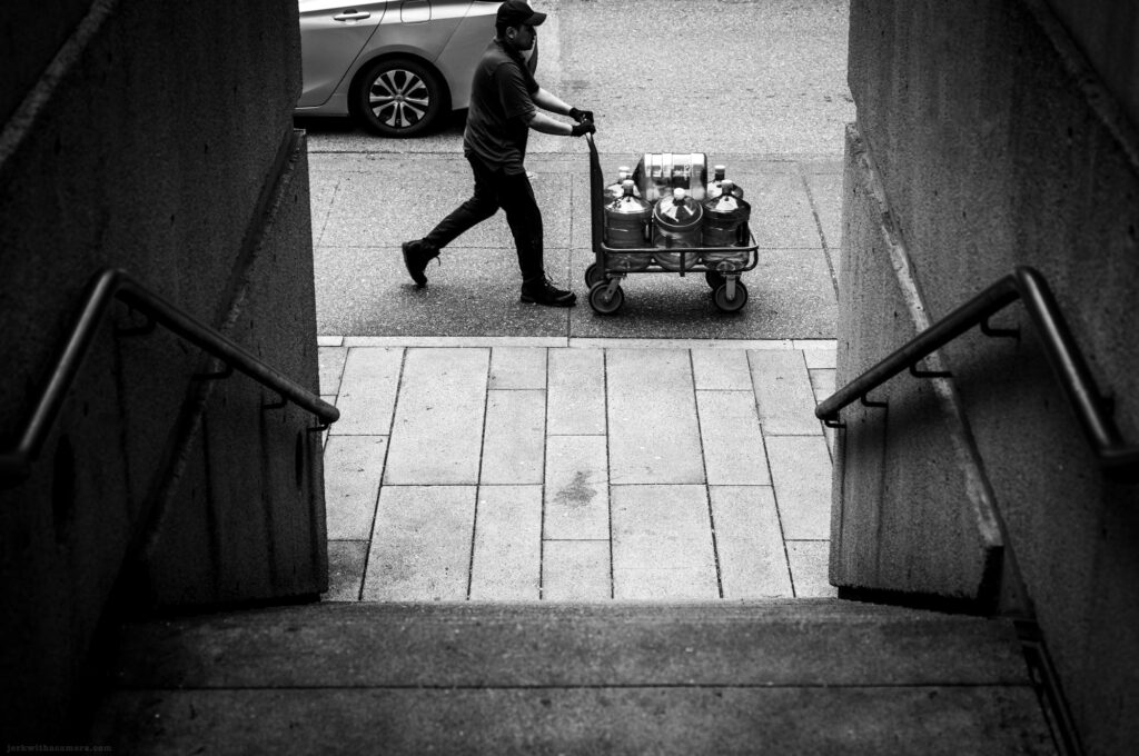 A man pushing a cart of metal canisters on a city sidewalk