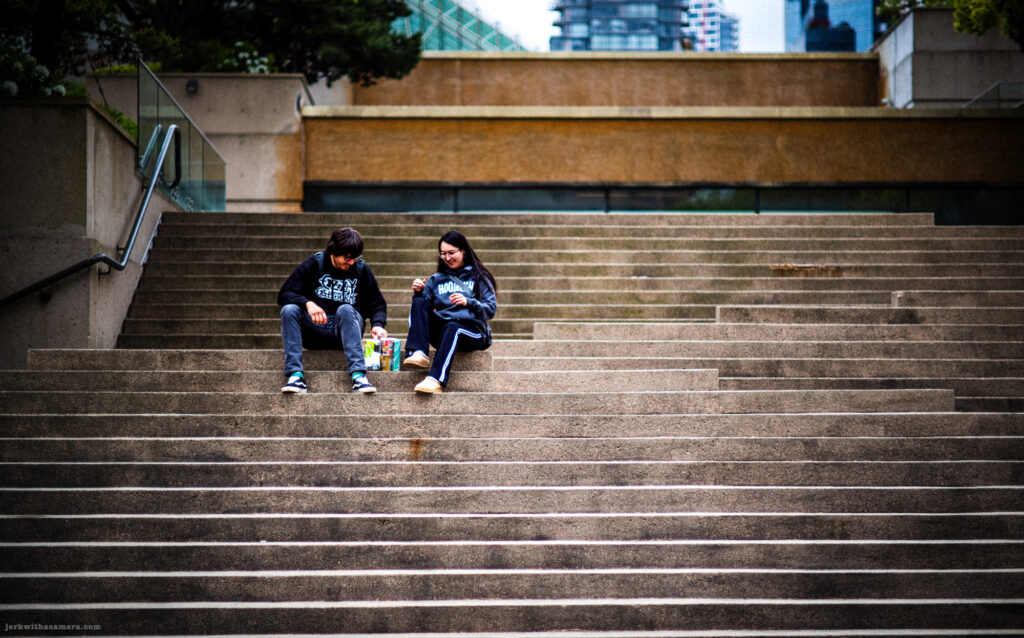 Two people sitting on wide concrete steps with snacks between them