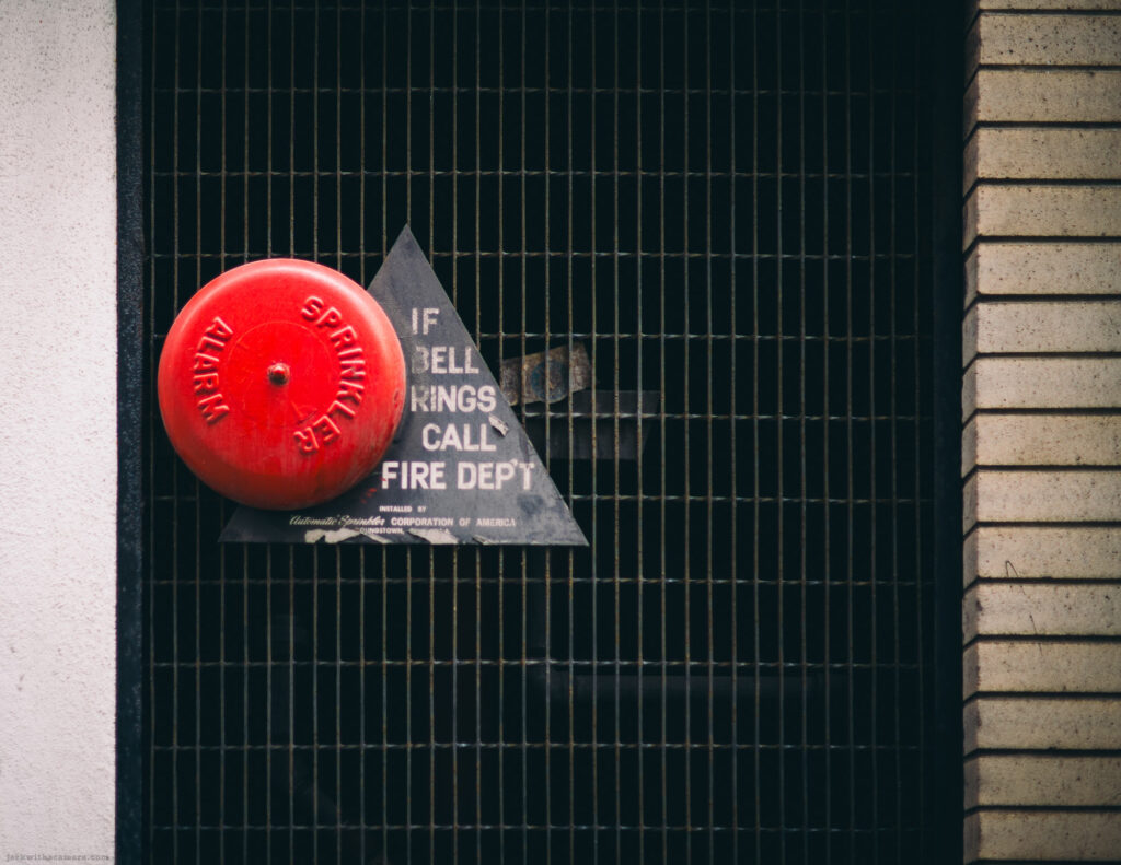 Red fire alarm bell with triangle sign on metal gate