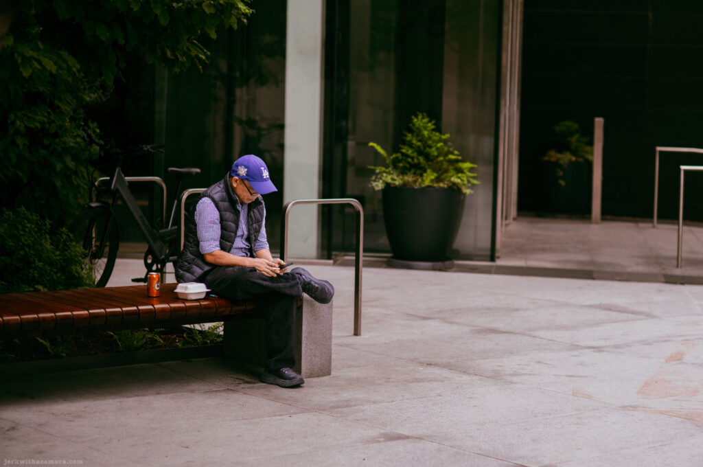 Man in a blue cap looking at his phone while seated on a bench