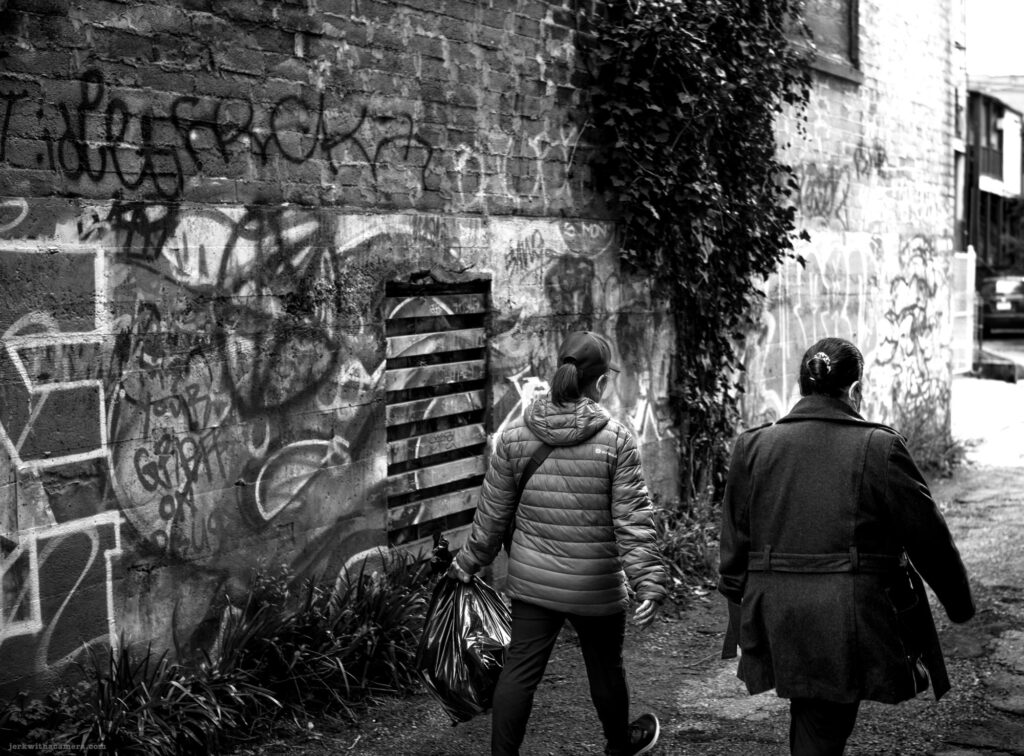 Two people walking down a graffiti-covered alley with a trash bag