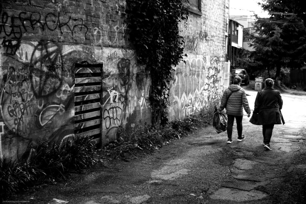 Two people walking down a graffiti-covered alley with a trash bag
