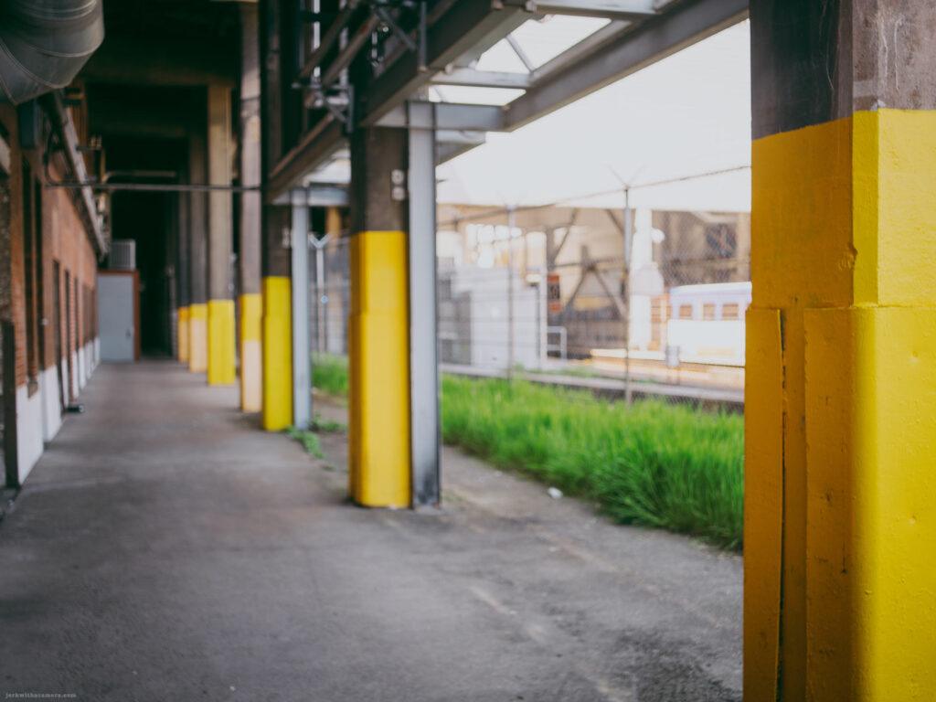 Yellow-painted columns along a Train Station beside a chain-link fence
