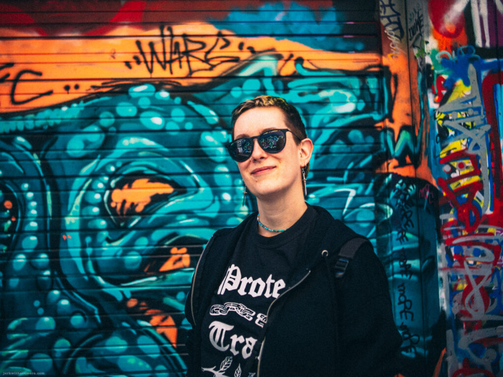 Kay posing in front of a blue and orange graffiti wall