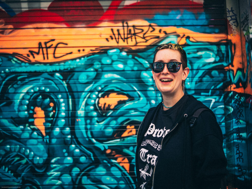 Kay posing in front of a blue and orange graffiti wall