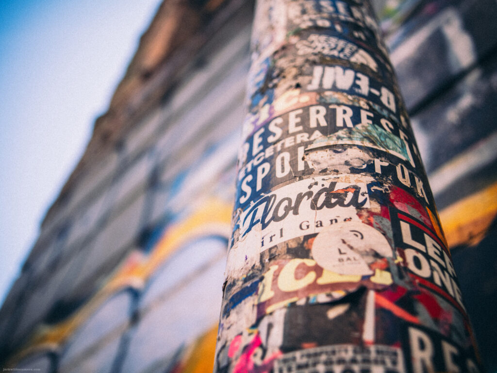 Close-up of a sticker-covered pole with graffiti in the background