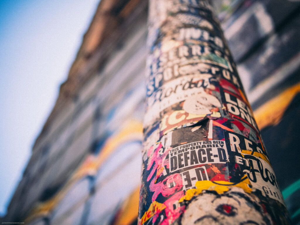 Close-up of a sticker-covered pole with graffiti in the background