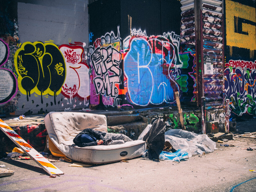 Discarded mattress and belongings with someone having a Nap in graffiti-covered alley