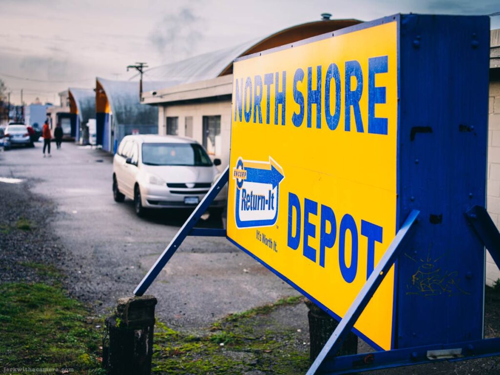 Return-It North Shore Depot sign along an industrial road with parked vehicles