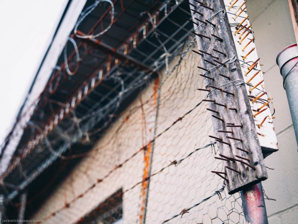 Spiked wooden barrier and wire mesh attached to a building wall in an industrial alley