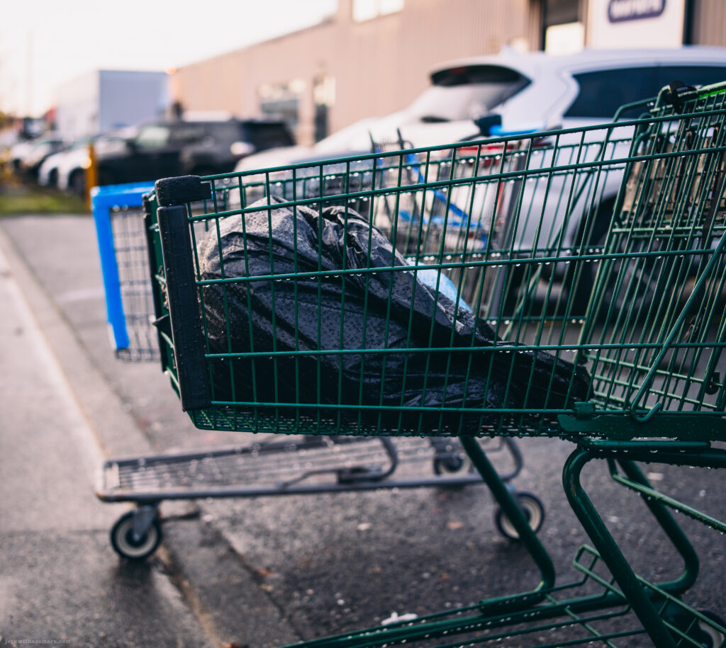 Shopping cart containing a covered item parked beside an industrial building
