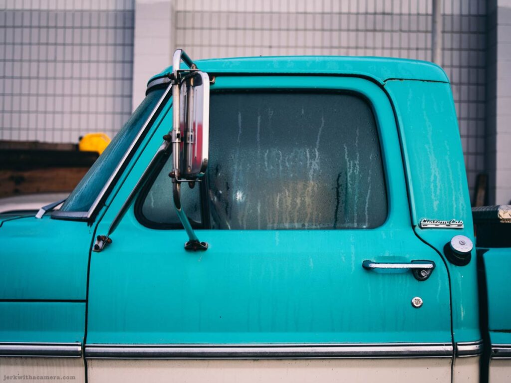 A turquoise and white vintage pickup truck parked along a city street.