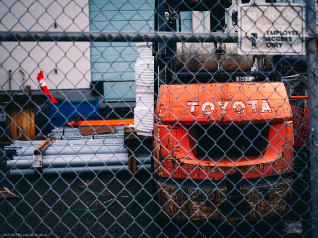 A Toyota forklift behind a chain-link fence in an industrial yard.