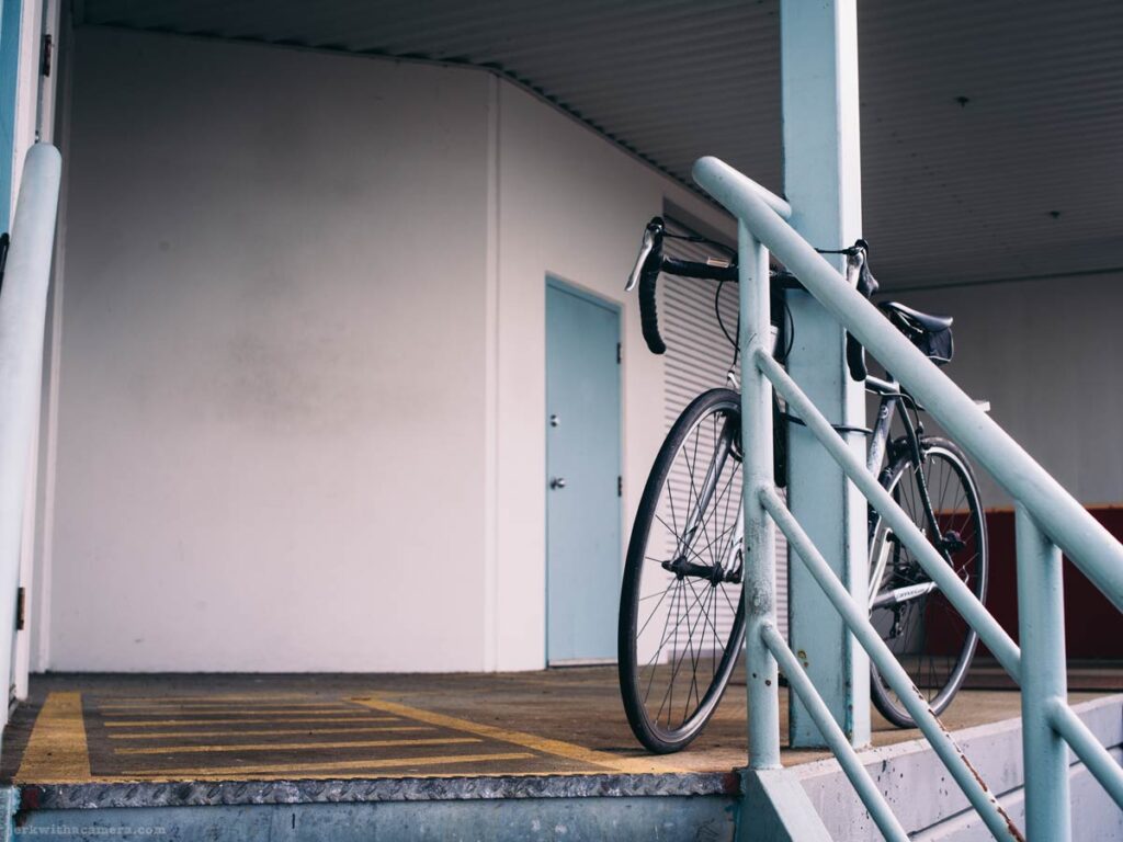 A road bicycle locked to a handrail outside an industrial building.