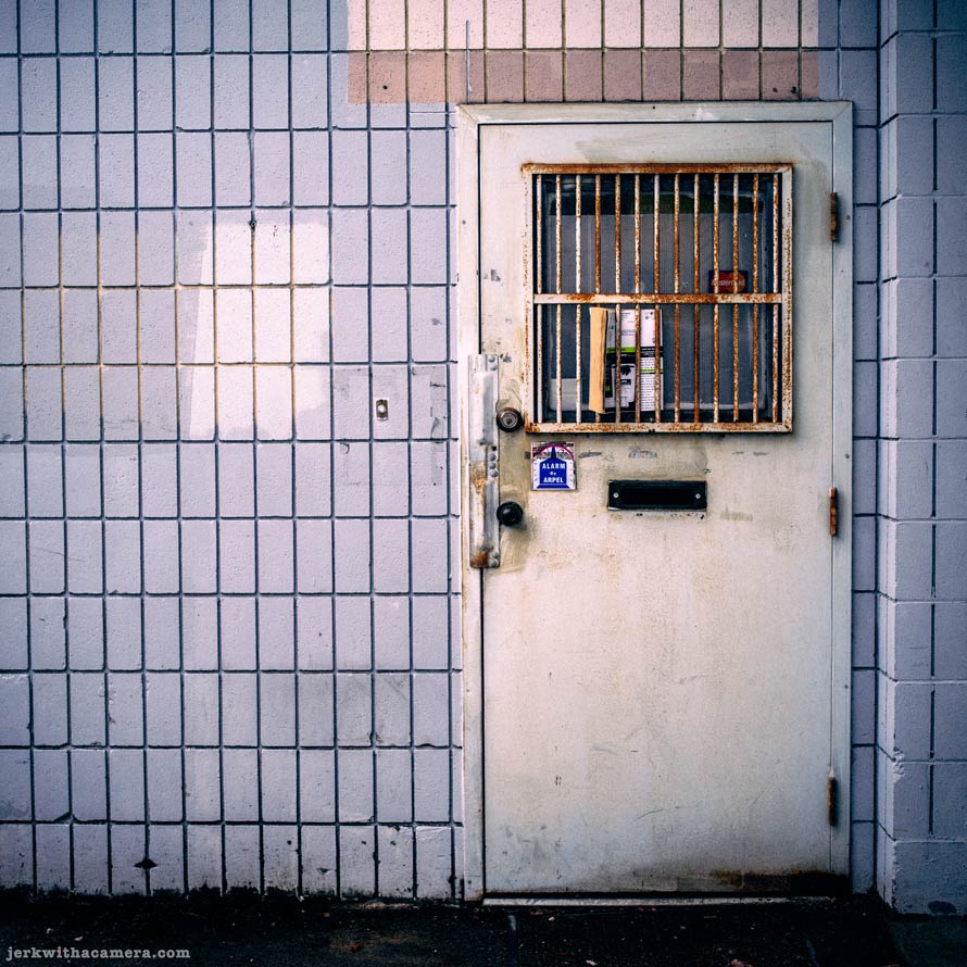 Metal door with barred window set in tiled exterior wall
