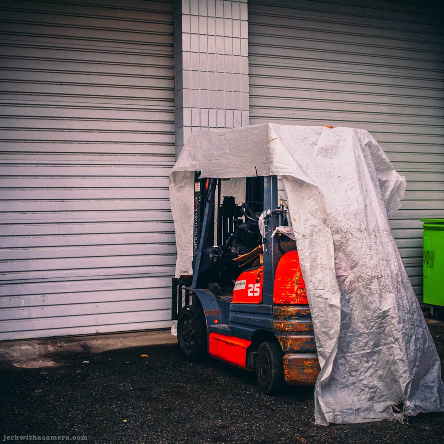 Forklift covered with tarp in front of closed roll-up doors