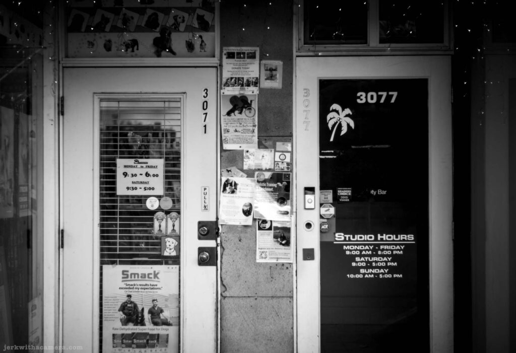 Two adjacent storefront doors with posted hours, flyers, and the street number 3077