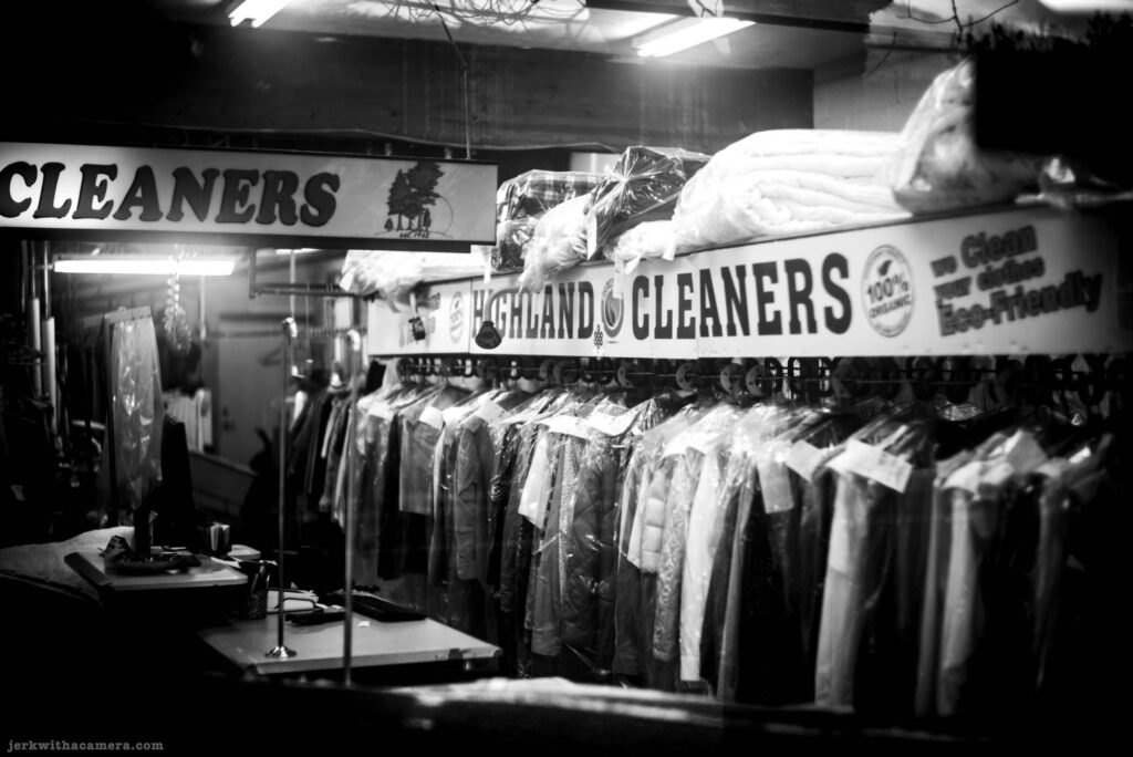 Interior of a dry cleaner with clothing hanging in plastic and a Highland Cleaners sign