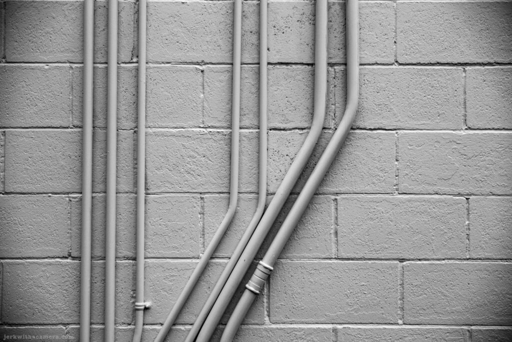 Painted brick wall with several vertical and curved conduit pipes