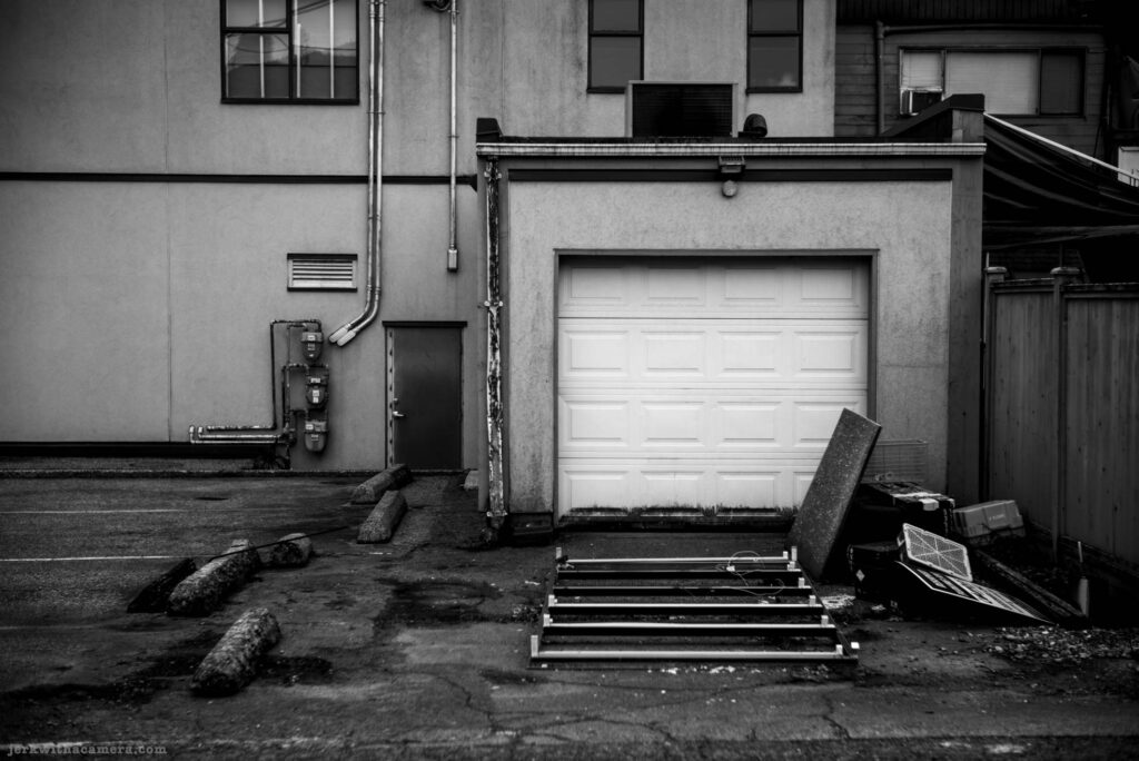 Rear of a building with a garage door, utility meters, and discarded metal frames in a parking lot