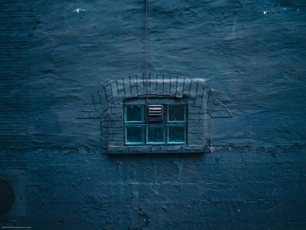 Small glass block window set into dark blue painted brick wall