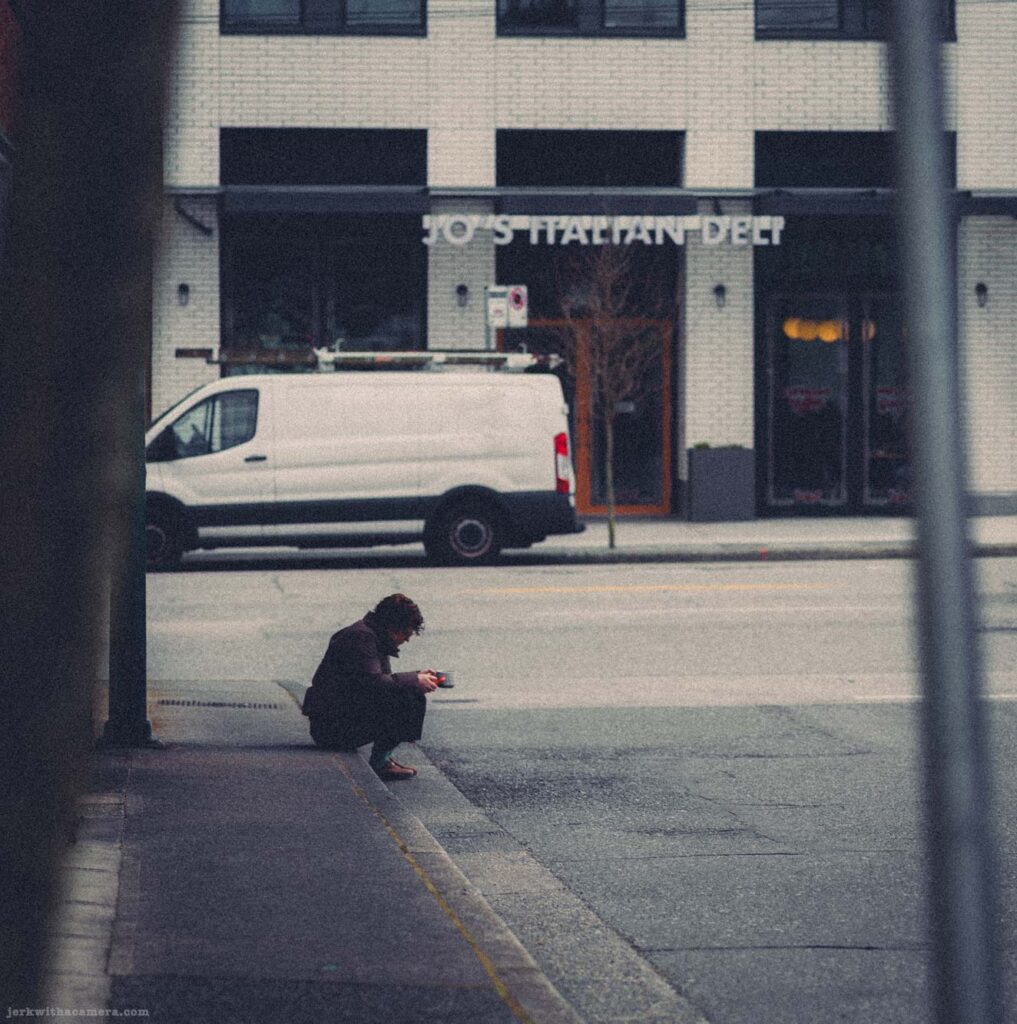 Distant figure sitting near curb viewed through dark foreground framing