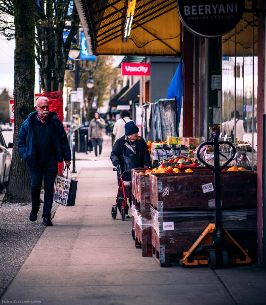 Sidewalk scene with grocery display and pedestrians passing storefronts