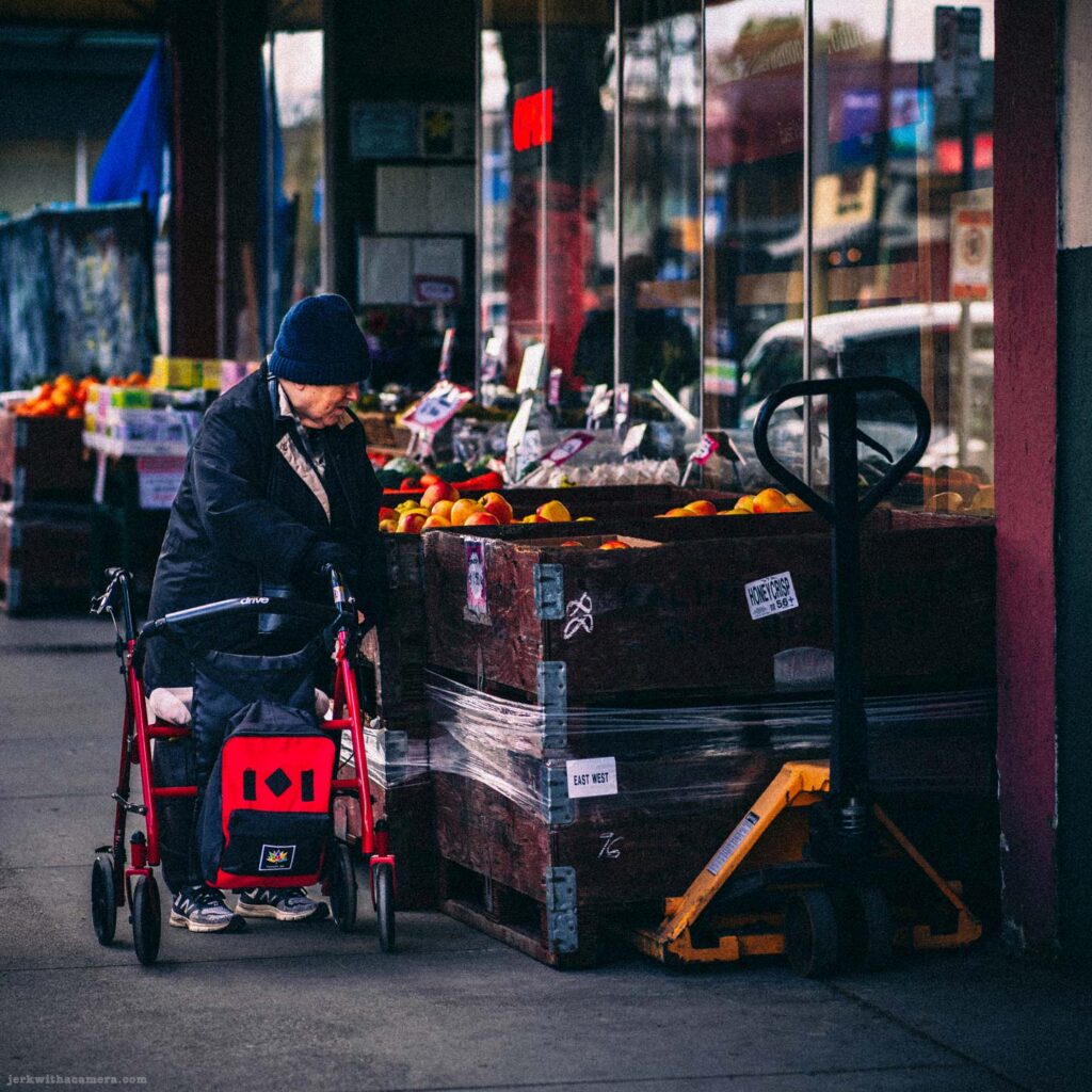 Elderly person with red walker browsing produce outside grocery store