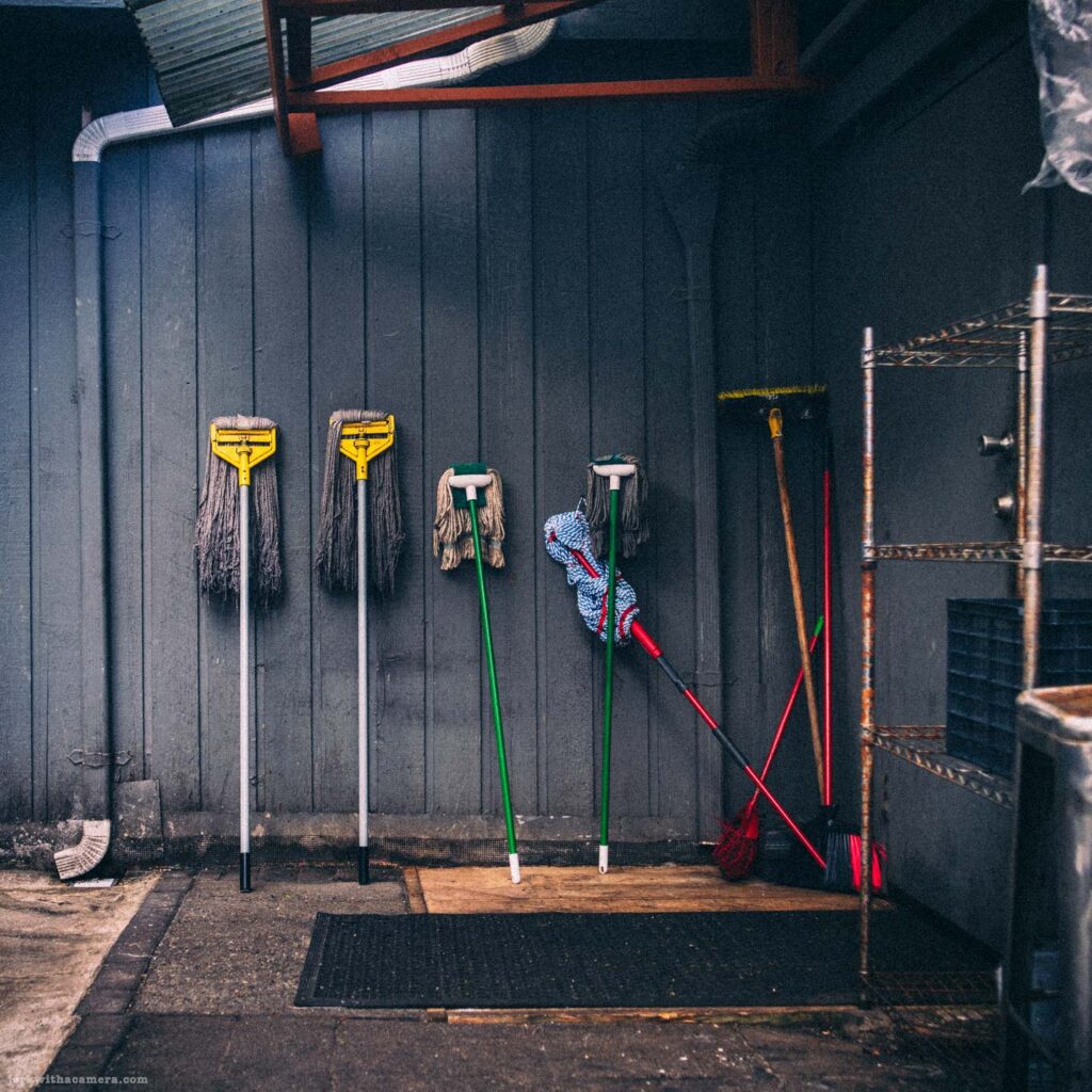 Collection of mops and cleaning tools lined against dark wall