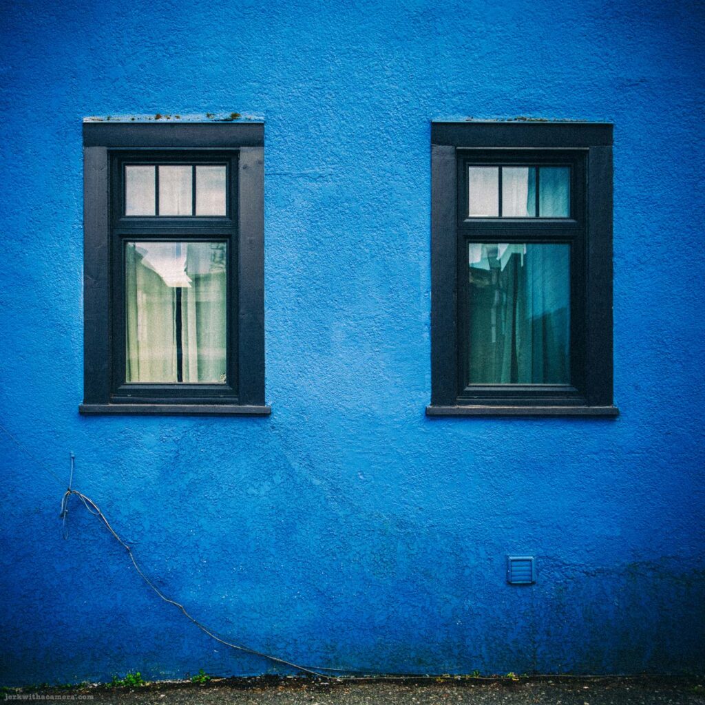 Two windows set into bright blue textured exterior wall