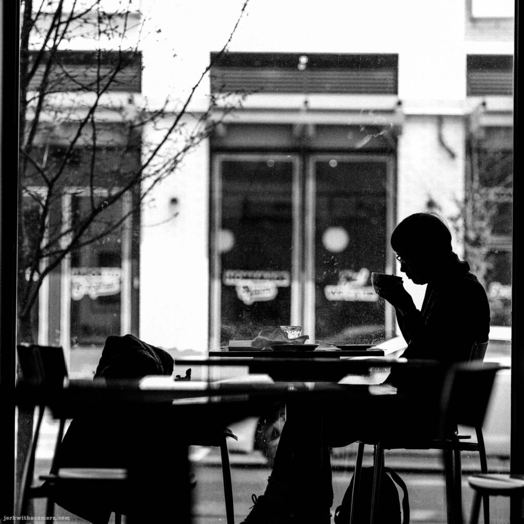 Silhouette of person drinking from bowl or cup inside cafe window