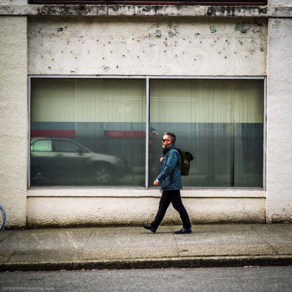 Man walking past large storefront windows with reflected vehicle in the glass
