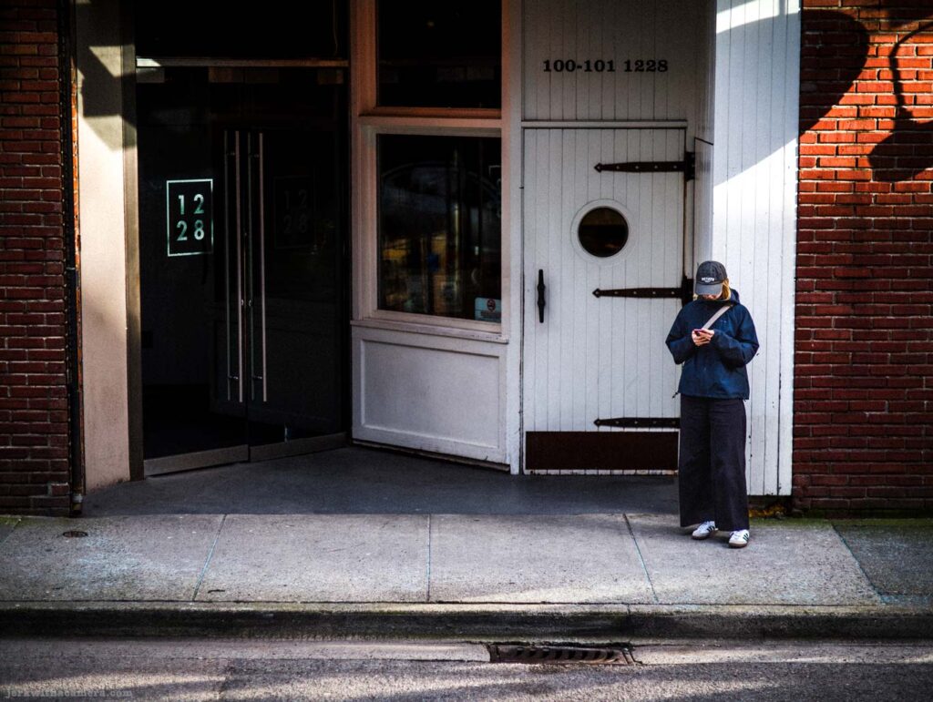 Person standing outside building entrance looking at phone